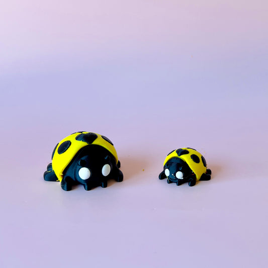 Two playful ladybug figures, one large and one small, with bright yellow shells and black spots, set against a soft pink back
