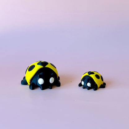 Two cute, stylized black and yellow ladybug figures with large eyes on a soft pastel background.