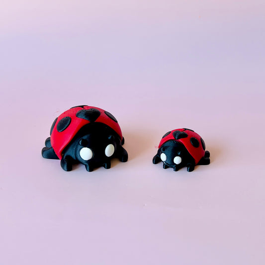 Two whimsical ladybug figures, one larger and one smaller, with red shells and black spots against a soft pink background.