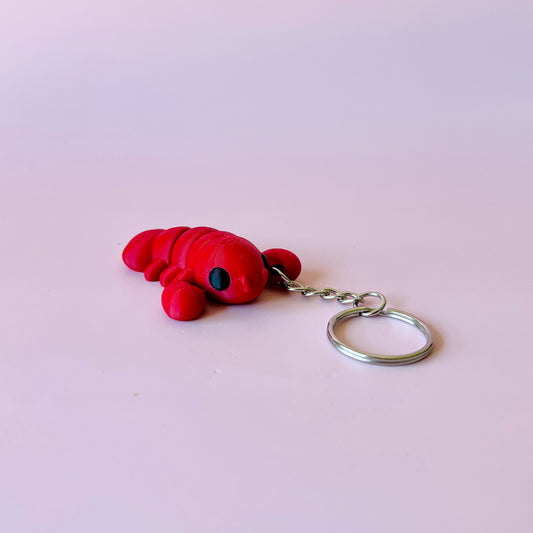 Red lobster keychain with black eyes, resting on a soft pink background.