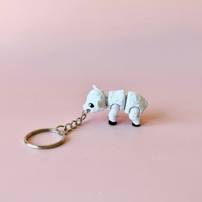 A small white animal figure with a keychain, featuring a fluffy texture and playful stance against a soft pink background.