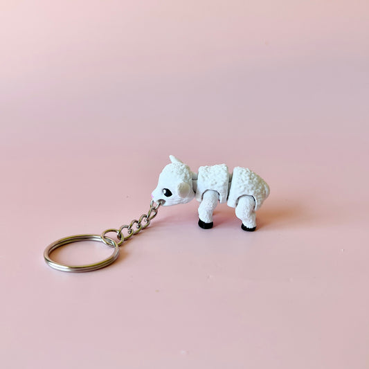 A small white animal figure with a keychain, featuring a fluffy texture and playful stance against a soft pink background.