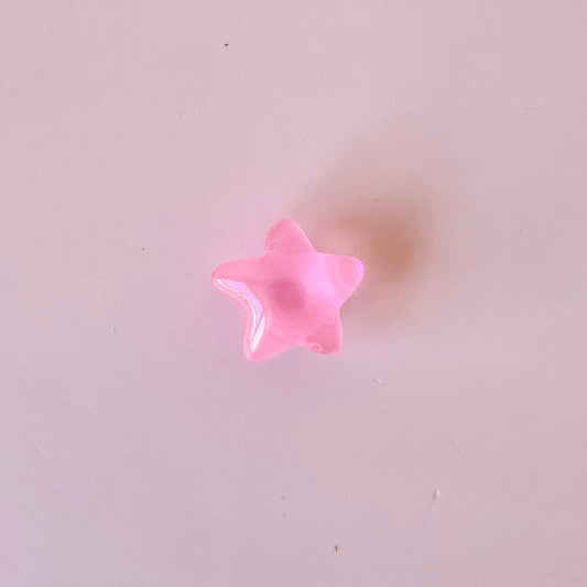 A glossy pink star shape rests on a soft pastel background, casting a subtle shadow.
