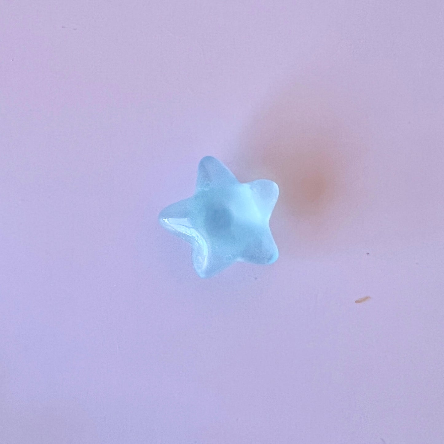 A translucent blue star shape resting on a soft pink surface, casting a gentle shadow beneath it.