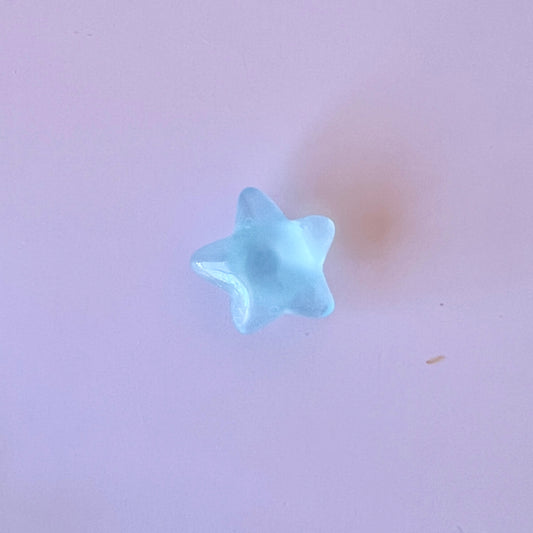 A translucent blue star shape resting on a soft pink surface, casting a gentle shadow beneath it.