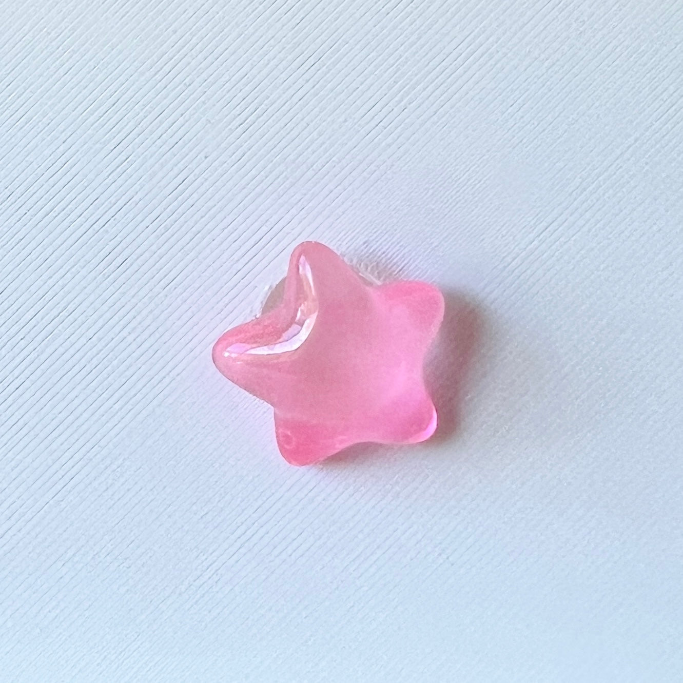 A shiny pink star-shaped object resting on a textured white surface, reflecting light subtly.