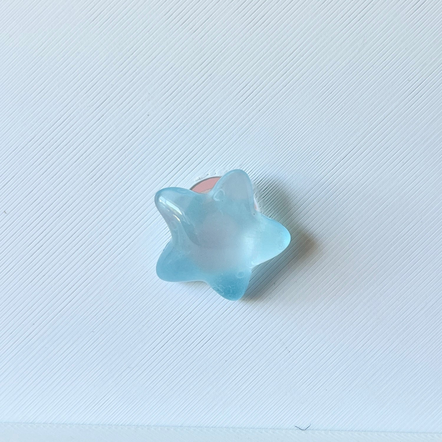 A translucent blue star-shaped piece rests on a textured white background, reflecting light softly.