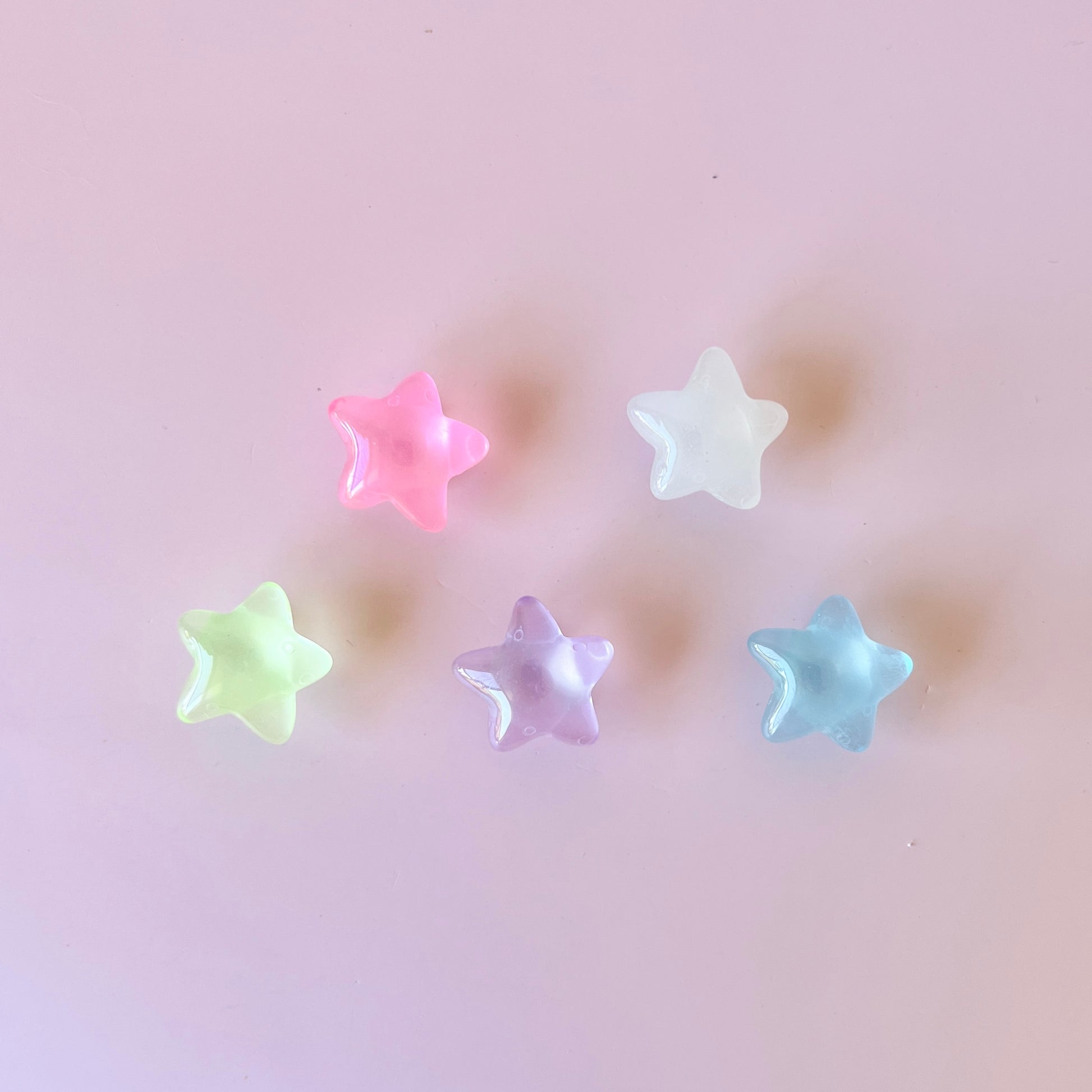 Five colorful star-shaped pieces in pastel shades on a soft pink background.