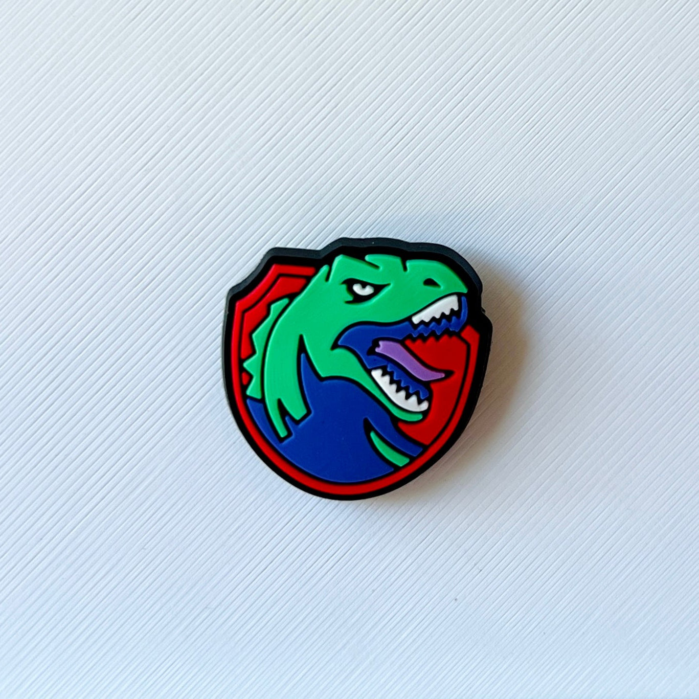 Colorful dinosaur emblem featuring a fierce expression, outlined in black, set against a textured white background.