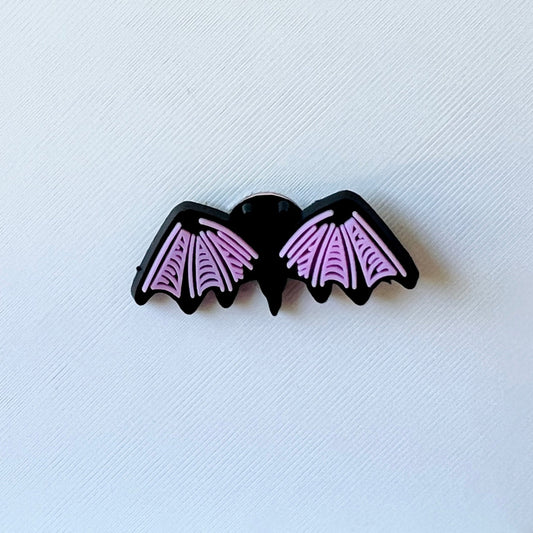 A black bat with pink wings, featuring detailed patterns, rests on a textured white background.