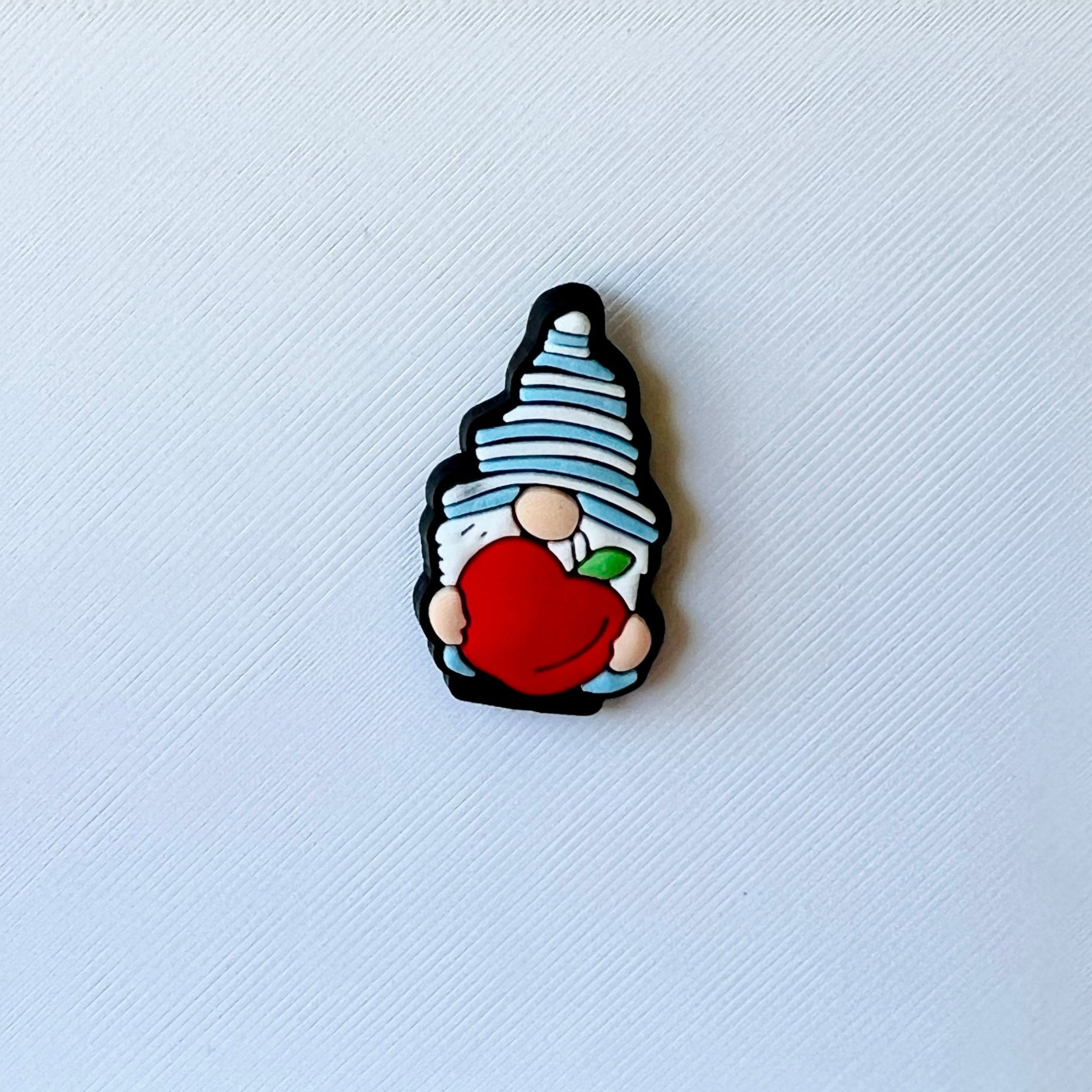 A whimsical character with a blue striped hat holds a bright red apple against a textured white background.