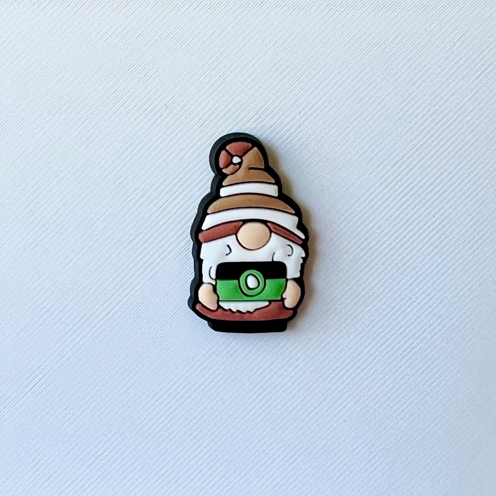 A whimsical character with a brown hat and white beard, holding a green camera against a textured white background.