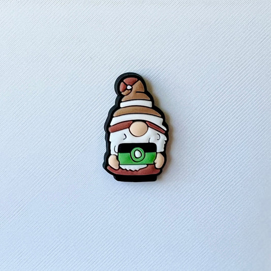 A whimsical character with a brown hat and white beard, holding a green camera against a textured white background.
