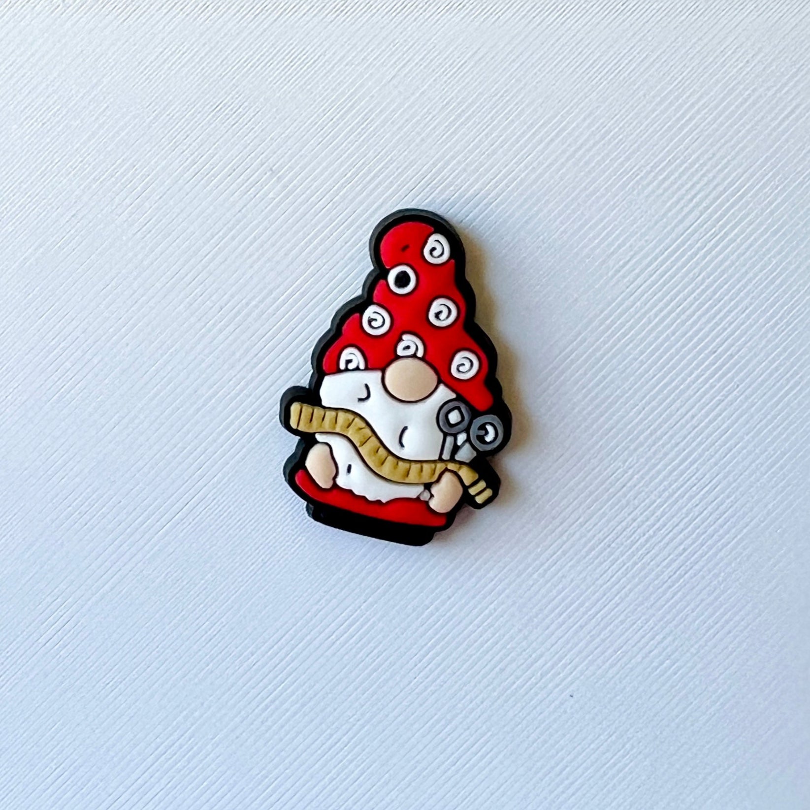 A whimsical figure with a red hat adorned with spirals, holding a tool and a measuring tape, set against a textured white bac