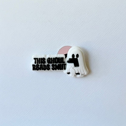 A playful ghost character holding a book, accompanied by the text "THIS GHOUL READS SMUT" in bold lettering.
