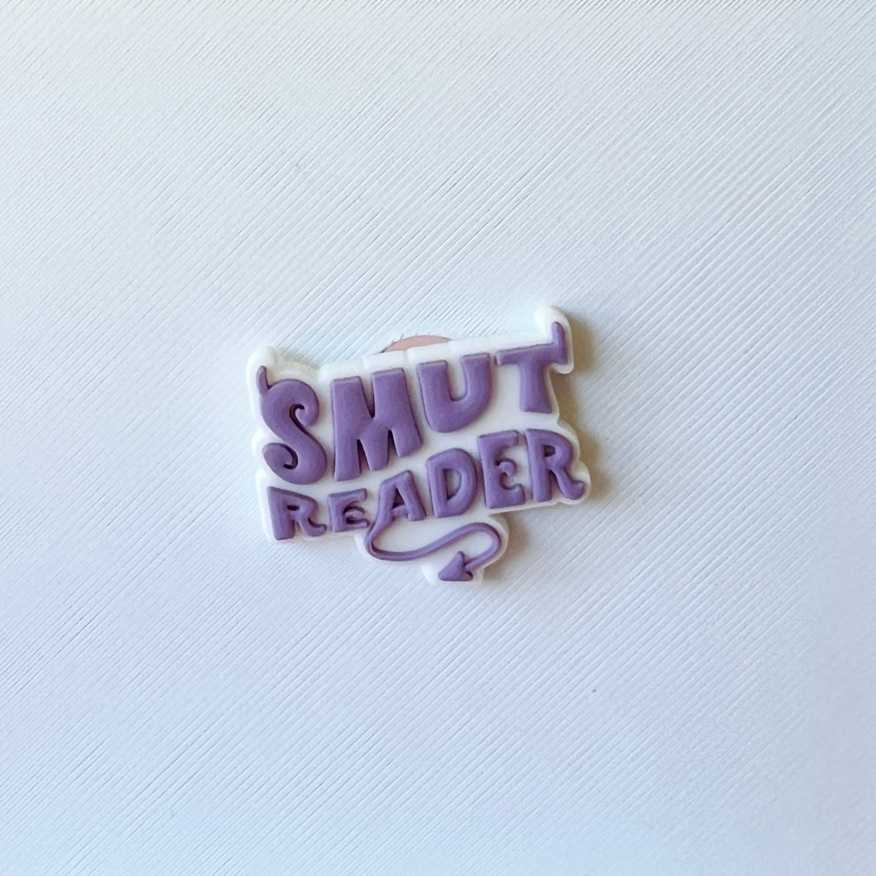 A playful purple and white badge with "SMUT READER" in bold, whimsical font against a textured white background.