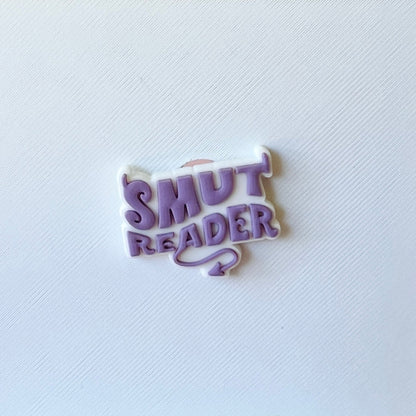 A playful purple and white badge with "SMUT READER" in bold, whimsical font against a textured white background.
