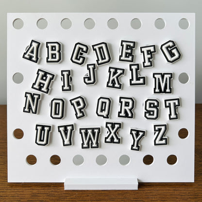Black and white alphabet shoe charms displayed on a white board, showcasing letters A to Z in a playful, bold style.