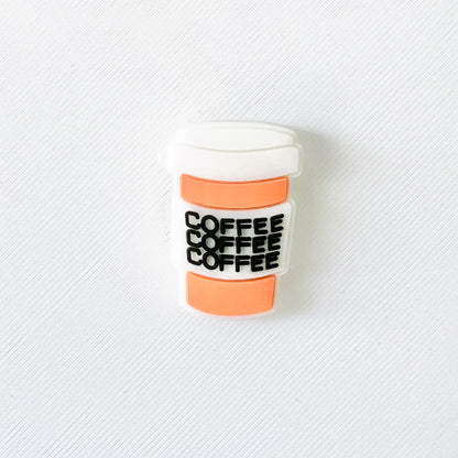 A two-tone shoe charm shaped like a coffee cup with "coffee" printed three times in bold black letters.