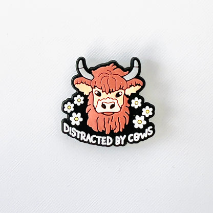 Brown Highland cow surrounded by white flowers with the phrase "Distracted by Cows" for a fun, quirky shoe charm.