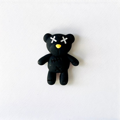Stitched black teddy bear charm with white cross eyes and yellow nose, perfect for adding edgy cuteness to shoes.