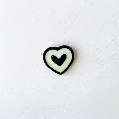 Layered black and white heart charm featuring a central black heart, white layer, and black outline on a textured background.