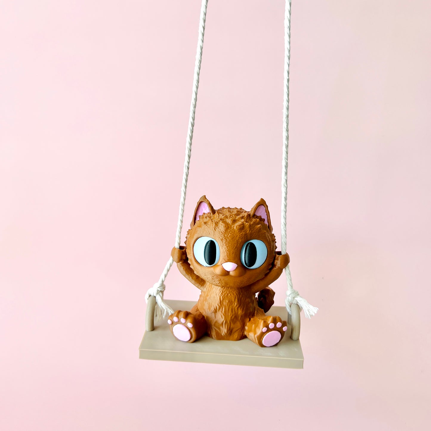 Adorable 3D-printed cat with big eyes happily swinging, showcasing charming details and tiny paws on a pastel background.