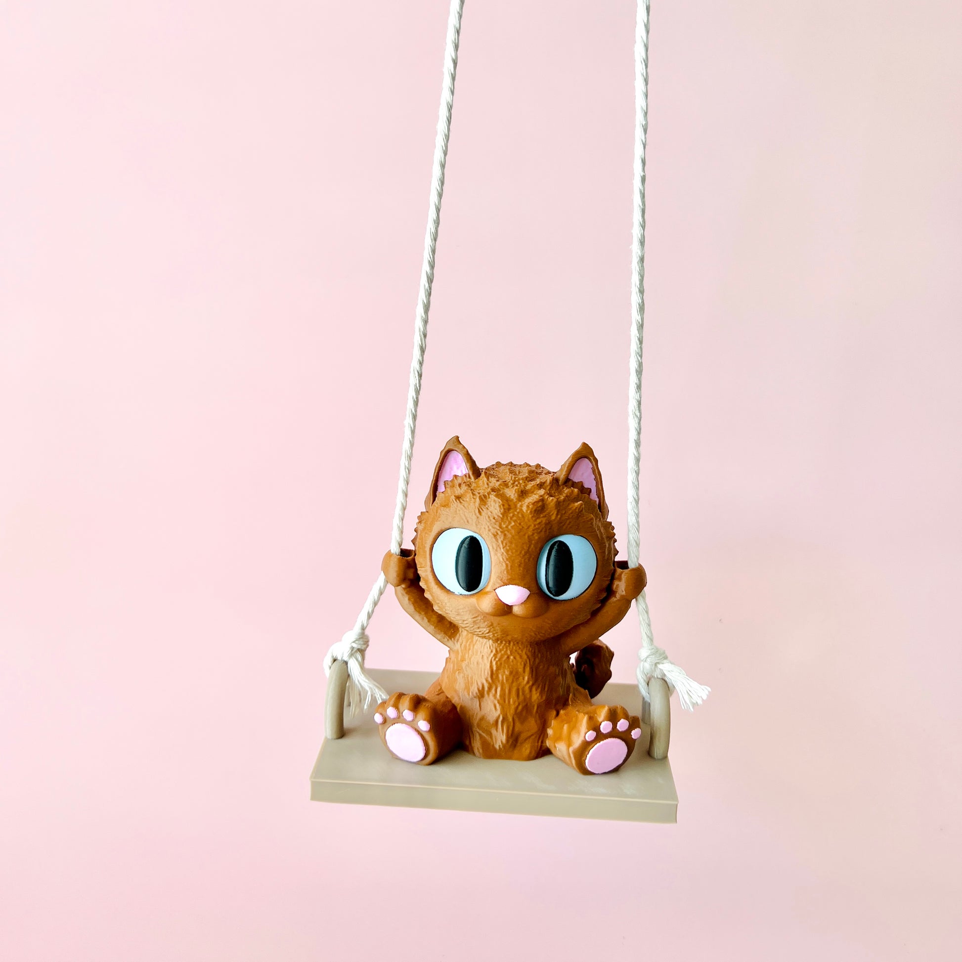 Adorable 3D-printed cat with big eyes happily swinging, showcasing charming details and tiny paws on a pastel background.