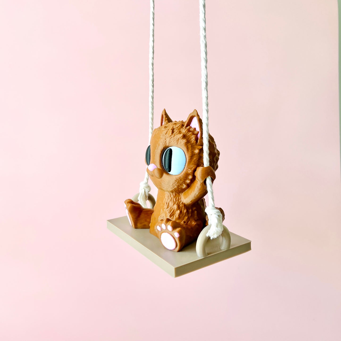 Adorable 3D-printed cat with big eyes happily swinging on a small platform, adding whimsy to any space.