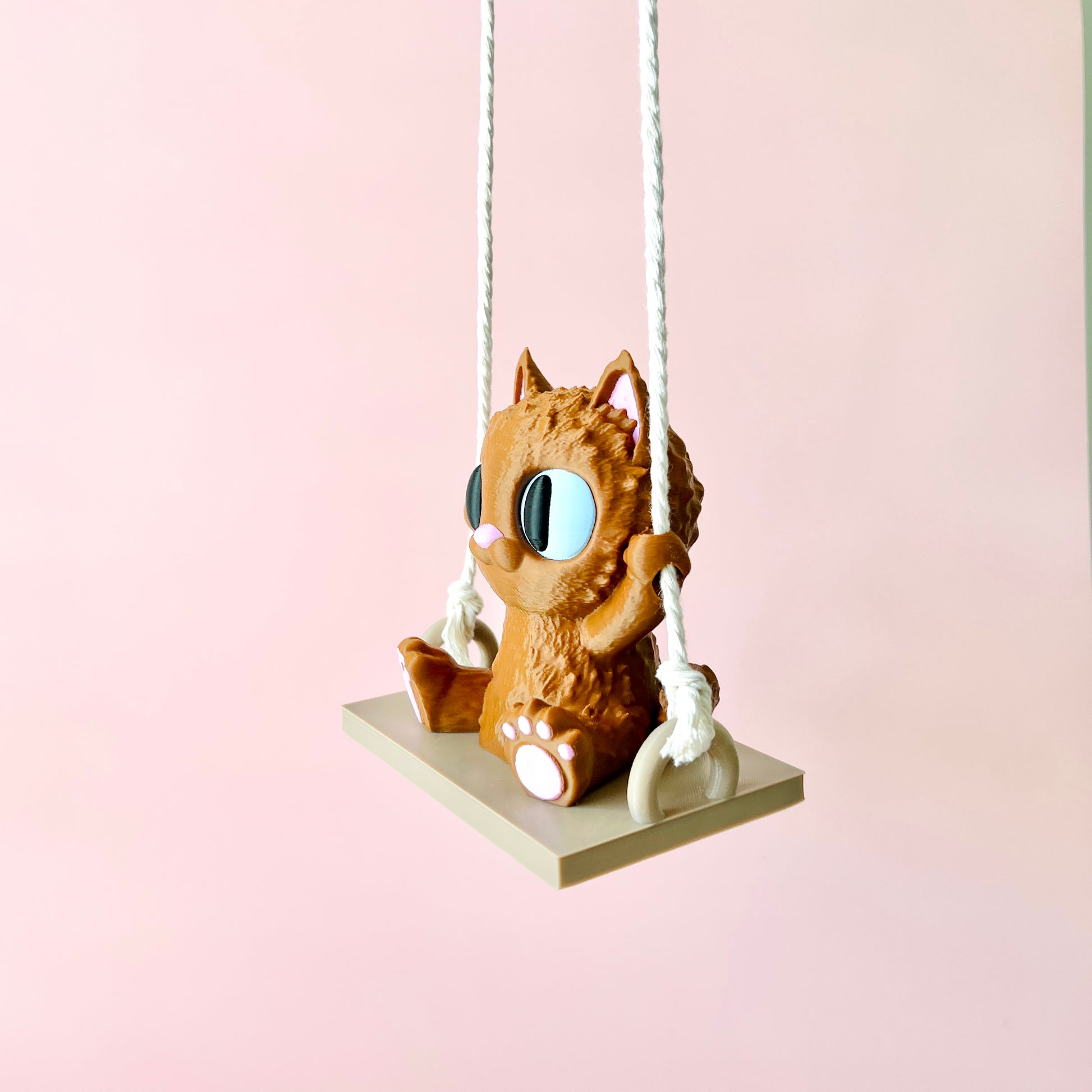 Adorable 3D-printed cat with big eyes happily swinging on a small platform, adding whimsy to any space.