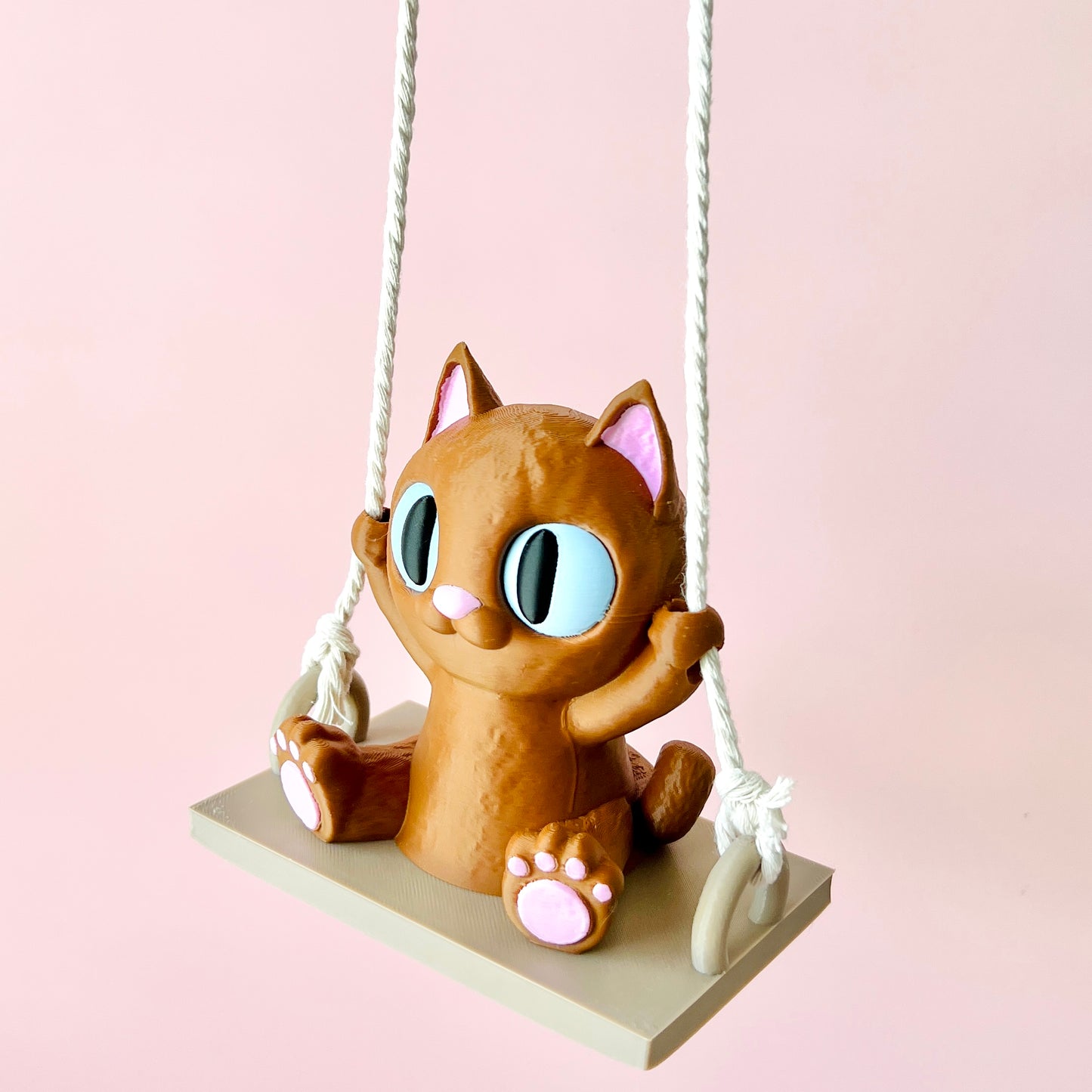 Adorable 3D-printed cat figurine swinging, with expressive eyes and tiny paws, adding whimsy to any space.