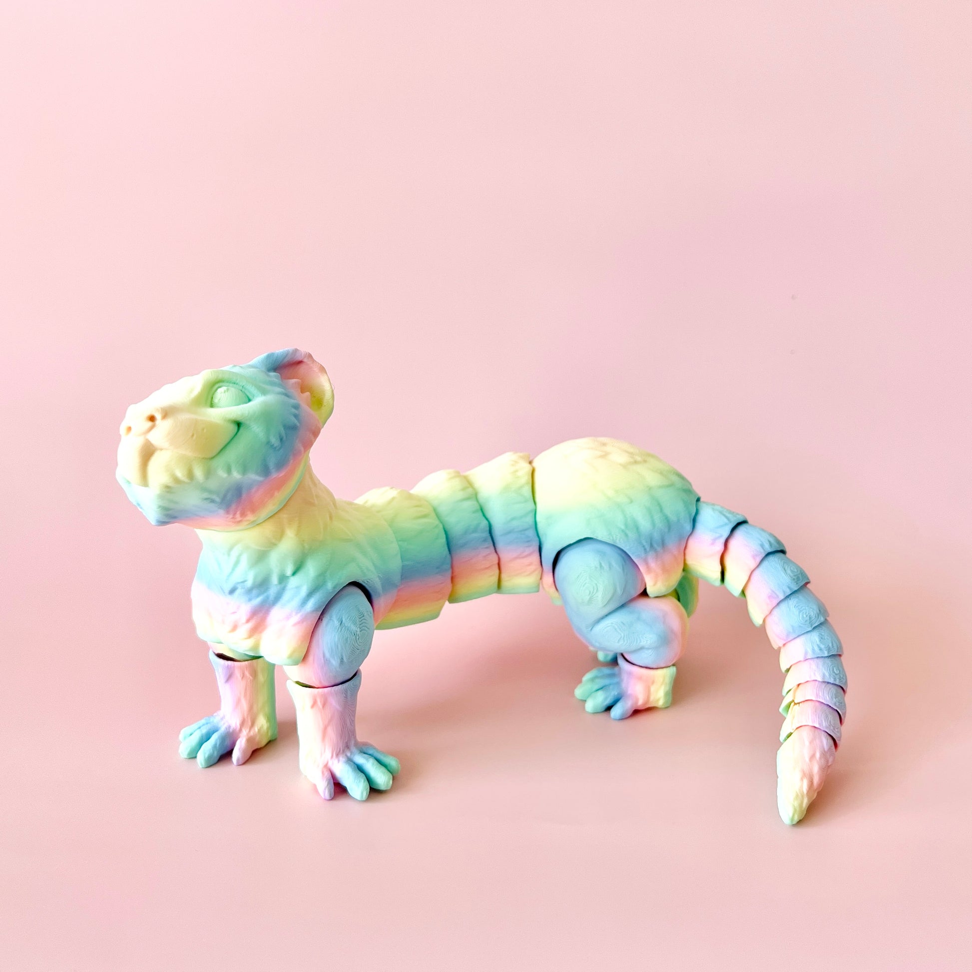 Colorful articulated ferret figurine with intricate details, playfully posed against a soft pink background.