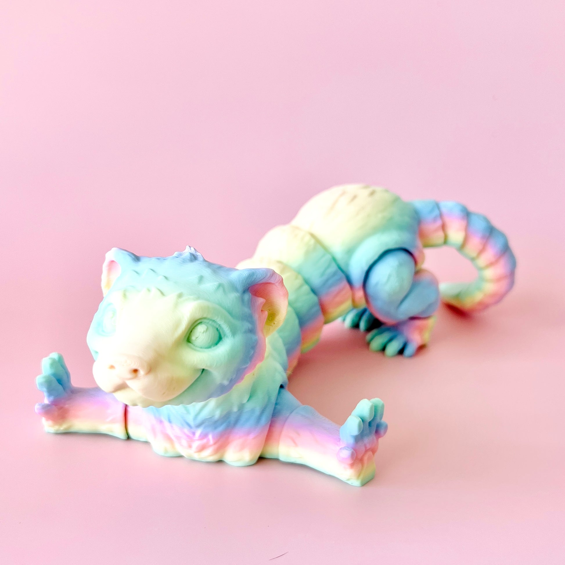 A colorful 3D-printed ferret figurine, showcasing intricate details and a playful pose against a soft pink background.