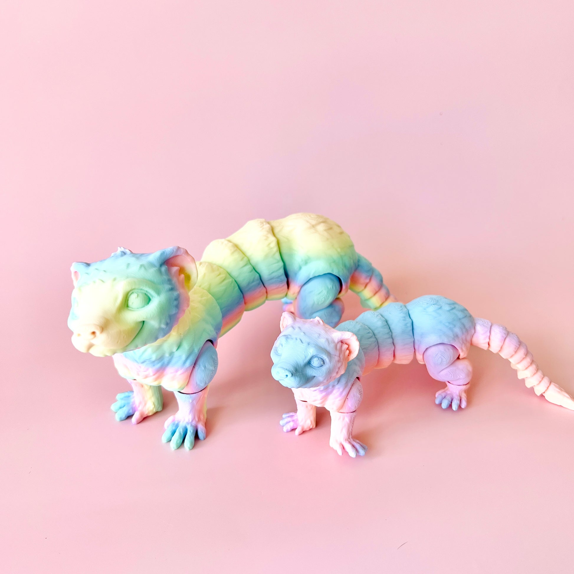 Colorful 3D-printed ferret figurines in playful poses, showcasing intricate details against a soft pink background.
