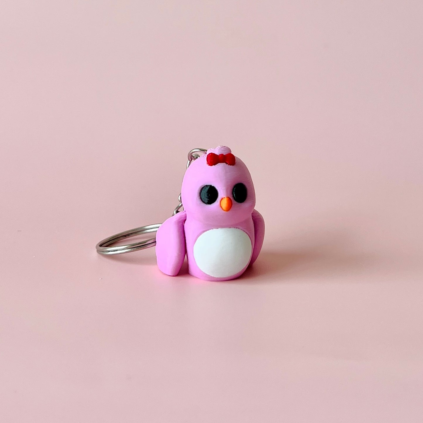 A small, pink bird figure with a red bow, black eyes, and white belly, resting on a soft pink background.