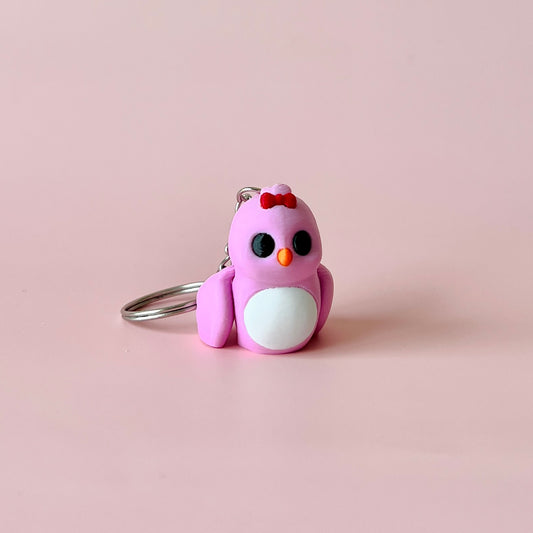 A small, pink bird figure with a red bow, black eyes, and white belly, resting on a soft pink background.