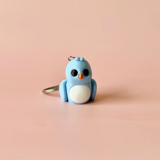A cute blue bird figure with a white belly and orange beak, set against a soft pink background.