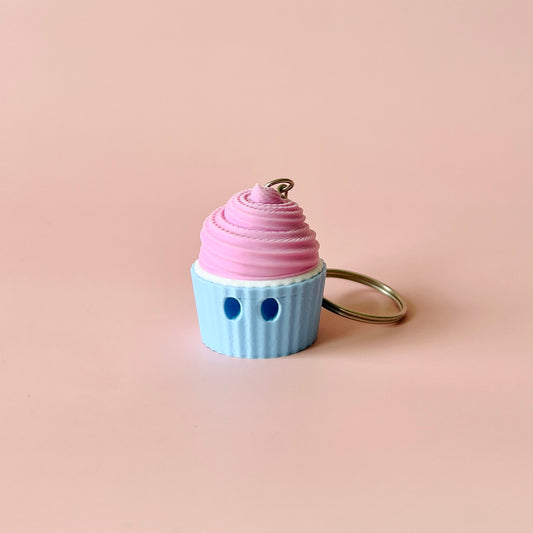 A pastel pink frosting atop a light blue cup, featuring two small blue eyes, set against a soft pink background.
