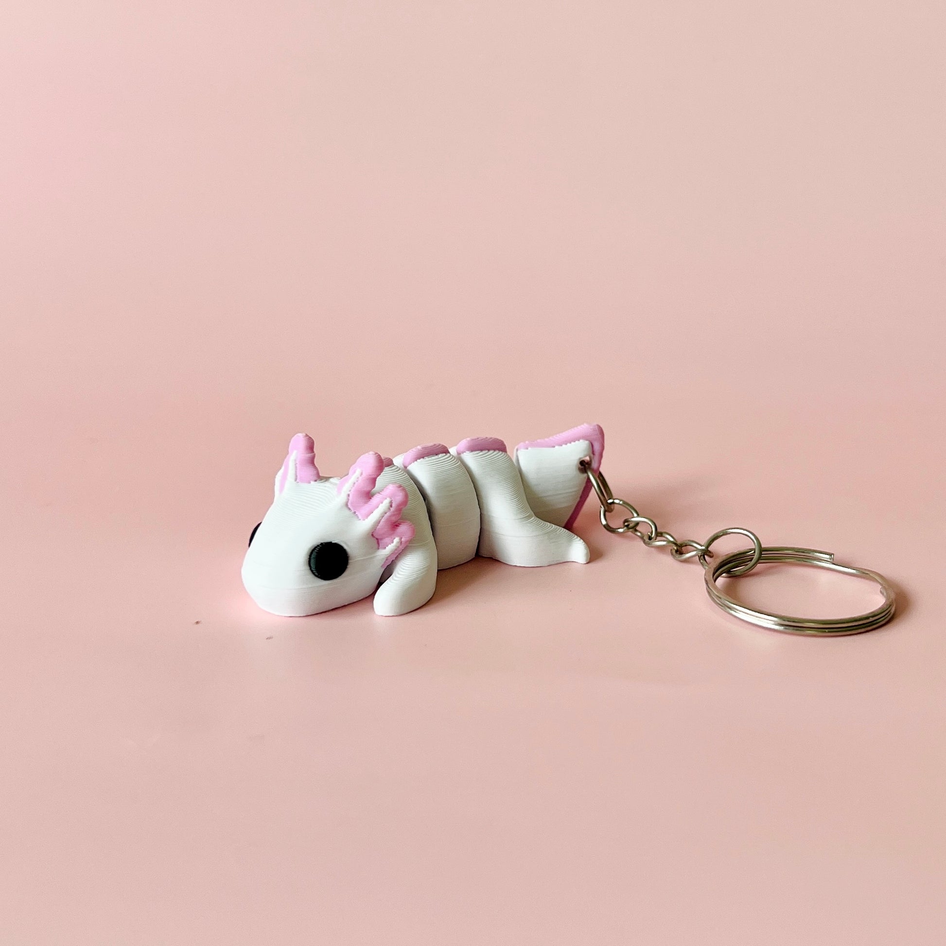 A whimsical creature in white and pink, featuring large eyes and a keychain attachment, set against a soft pink background.