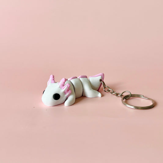 A whimsical creature in white and pink, featuring large eyes and a keychain attachment, set against a soft pink background.