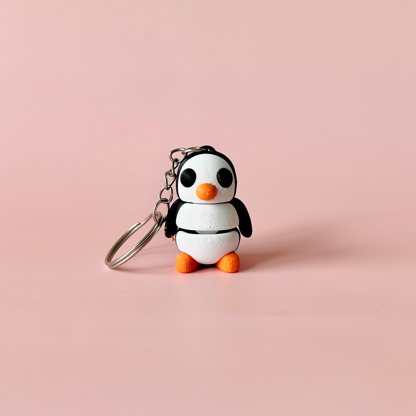 A cute, stylized penguin figure with orange accents and a keychain attachment against a soft pink background.