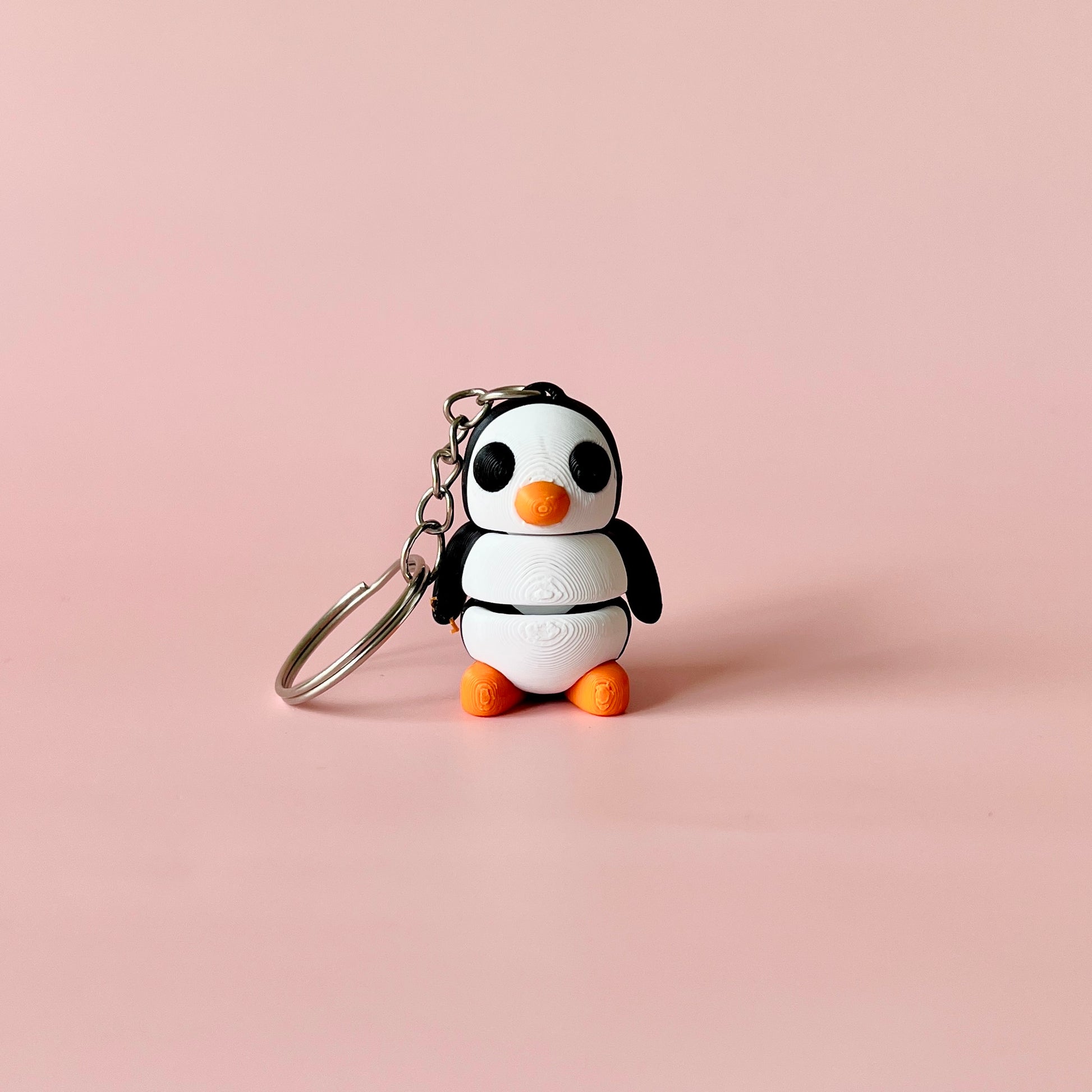A cute, stylized penguin figure with orange accents and a keychain attachment against a soft pink background.