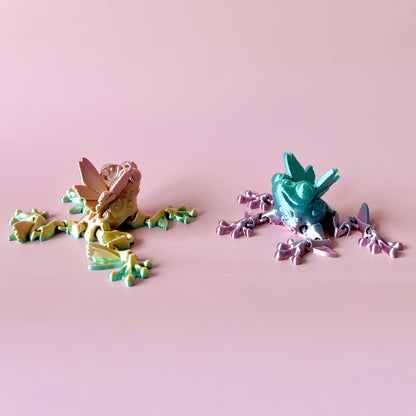 Whimsical Butterfly Frog figurines in pastel colors, showcasing delicate wings and playful designs against a soft pink backdr