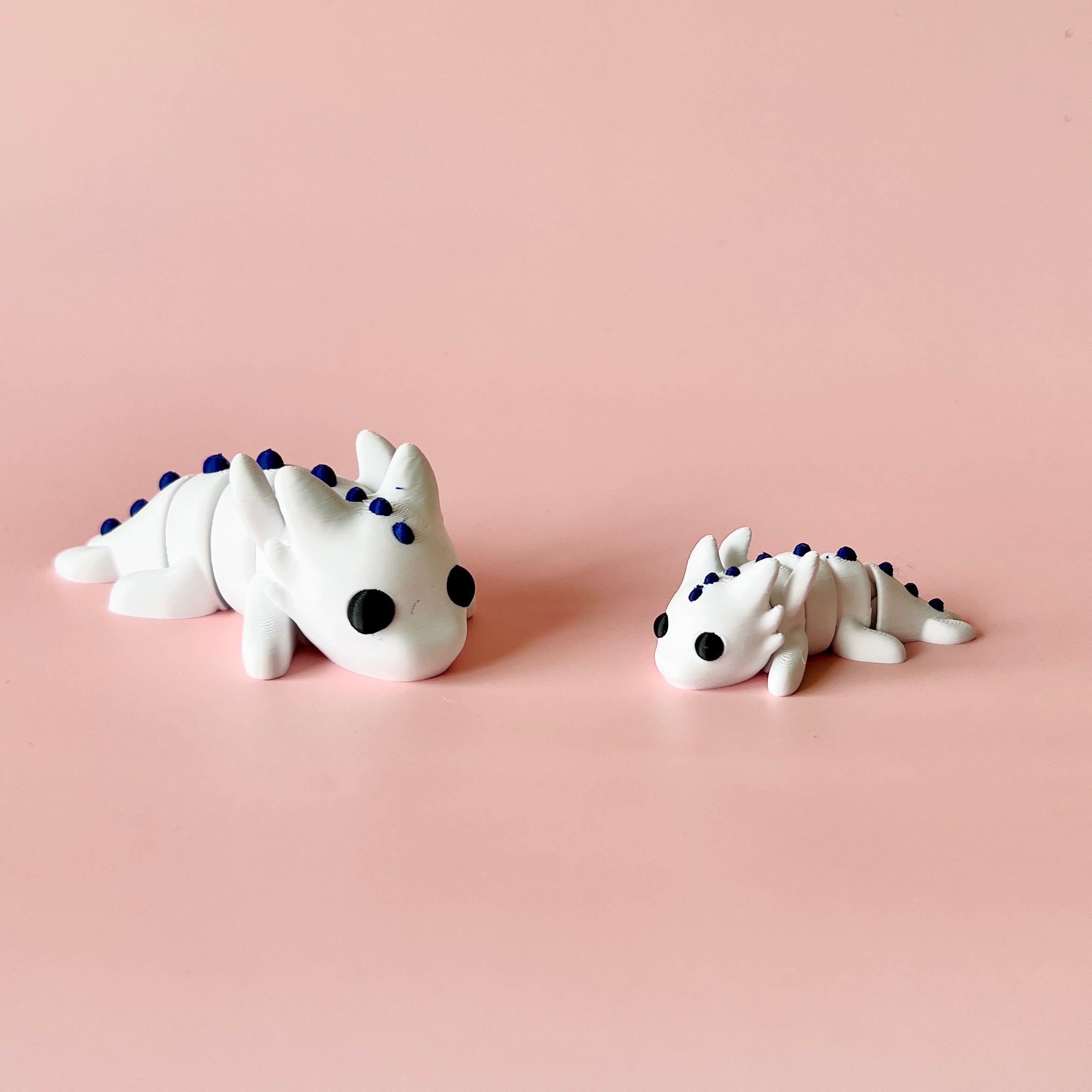 Two small white creatures with black eyes and blue spikes, resting on a soft pink background.