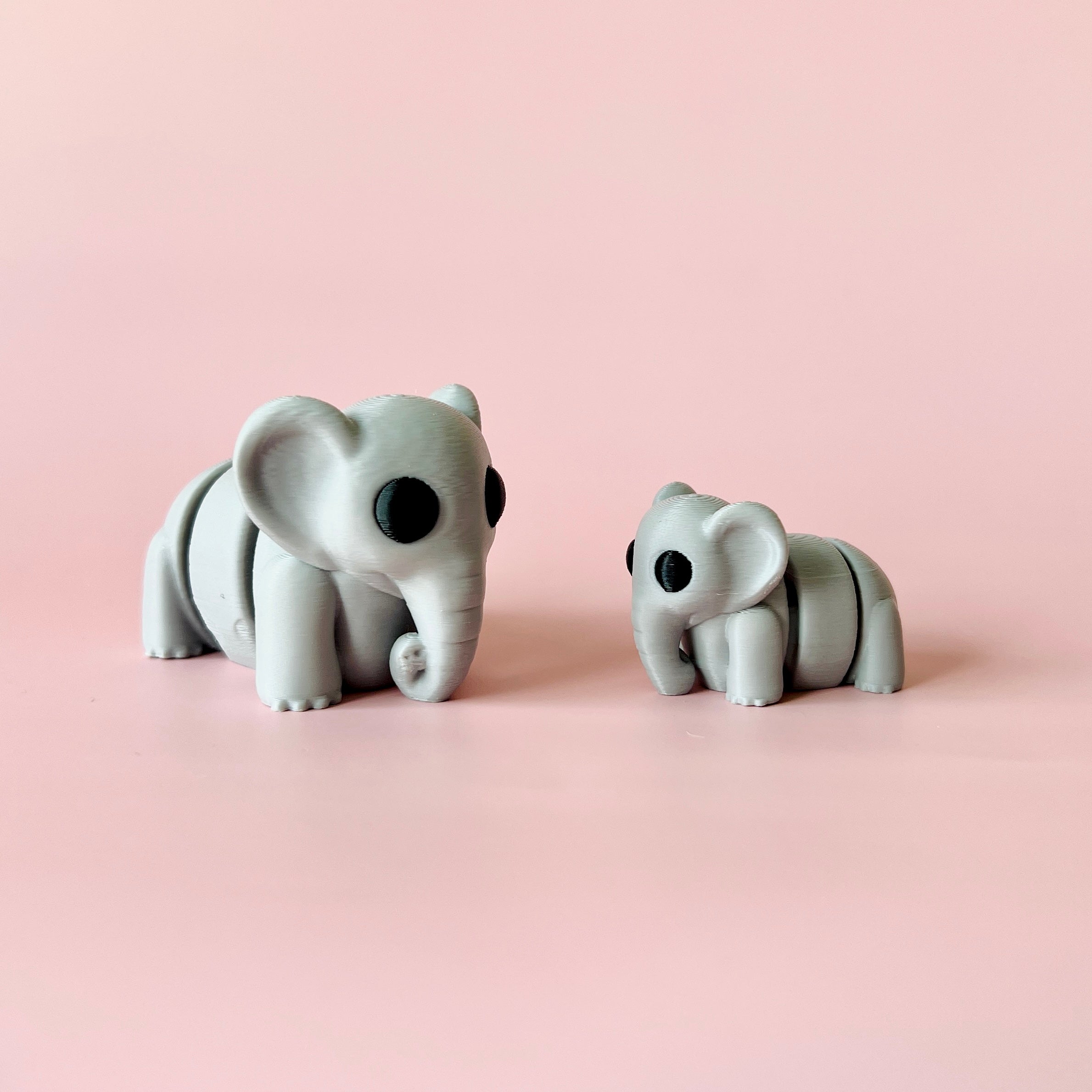 Two stylized gray elephants with black eyes, positioned on a soft pink background, showcasing their charming features.