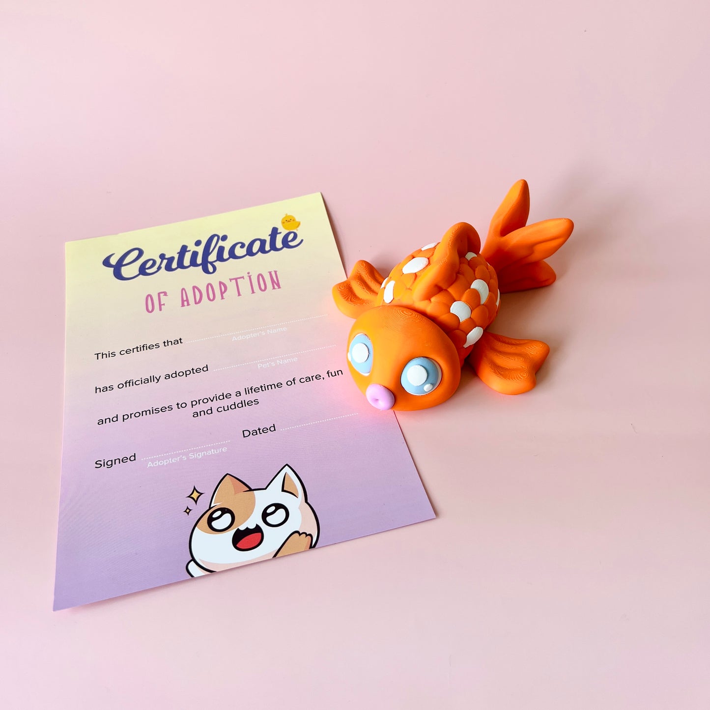 Colorful fish figurine beside a whimsical adoption certificate on a soft pink background.