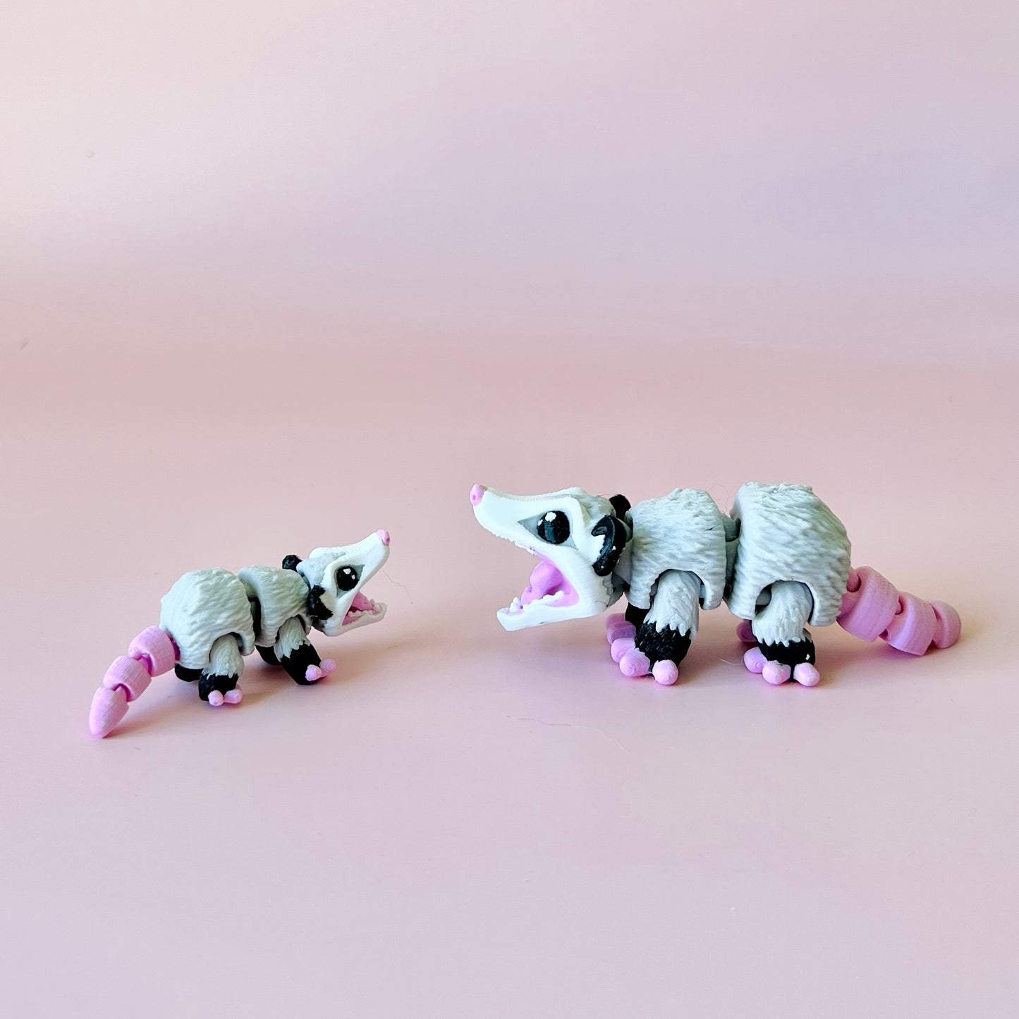 Two playful opossums with exaggerated features, one larger and one smaller, against a soft pink background.
