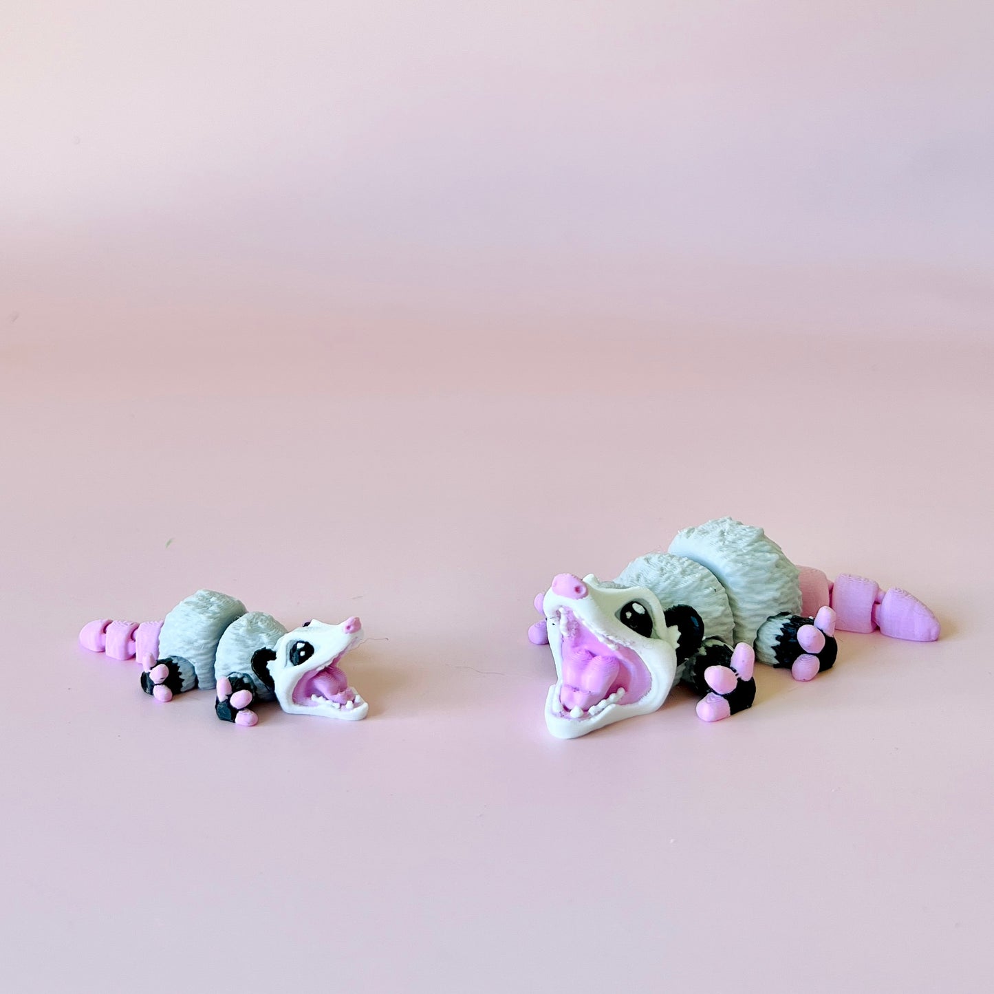 Two playful opossum figures, one large and one small, both with pink accents, against a soft pink background.