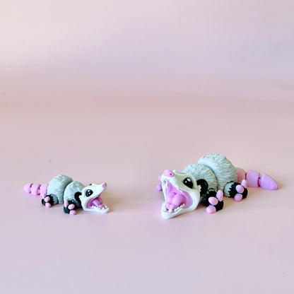 Two playful opossum figures, one large and one small, both with pink accents, against a soft pink background.