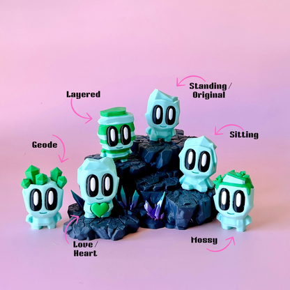 A playful arrangement of pastel green figures on textured black rocks, set against a soft pink background.